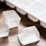 Ice cube tray filled with ice cubes and three loose ice cubes against dark wood.