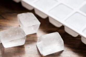 Ice cube tray filled with ice cubes and three loose ice cubes against dark wood.