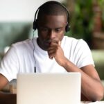 Young Black man sat in front of laptop while wearing headphones